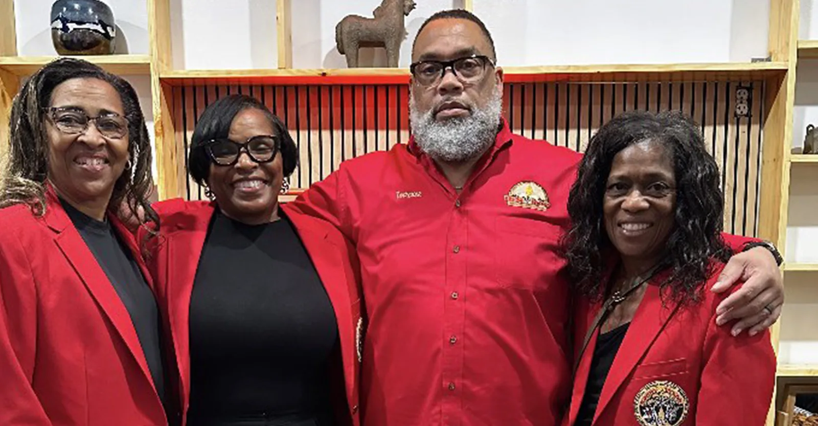 Four Krewe of Pyros members in red jackets and shirts at a community reception