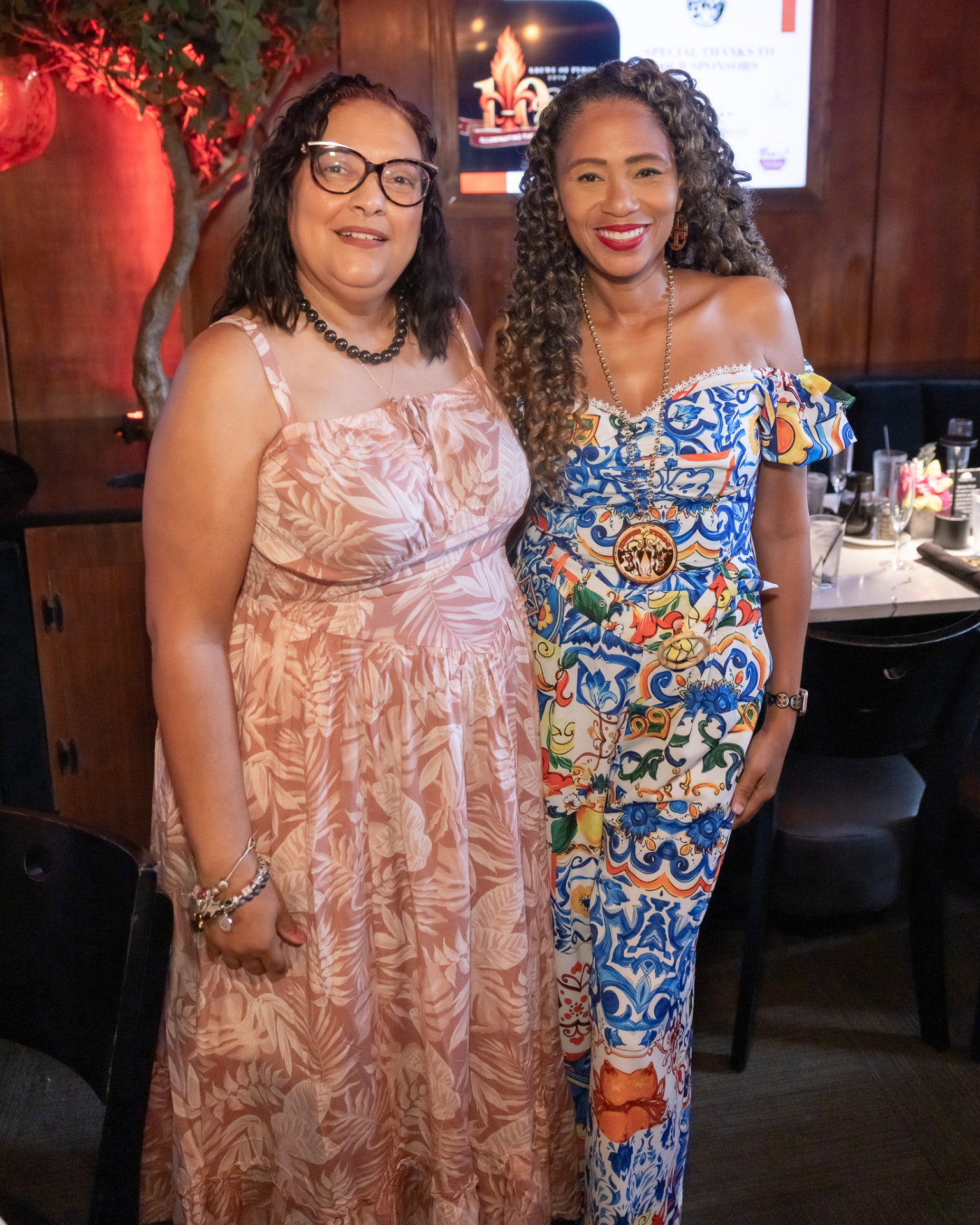 Two guests in colorful prints in front of the Krewe of Pyros 10 Years screen